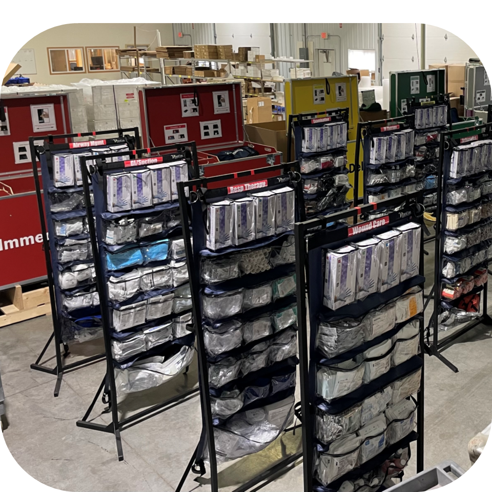 Multiple Upright Medical Organizers (UMOs) filled with emergency medical supplies staged in front of color-coded medical equipment chests preparing to support surge patient flow